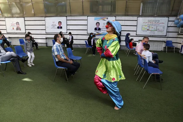 A clown performs as students and their parents wearing protective face masks to help prevent spread of the coronavirus attend the opening ceremony of the Hashtroudi school in Tehran, Iran, Saturday, September 5, 2020. Iran on Saturday opened the new school year after nearly seven months of closure as many expressed concern over a possible increase in infections of the Covid-19. (Photo by Vahid Salemi/AP Photo)