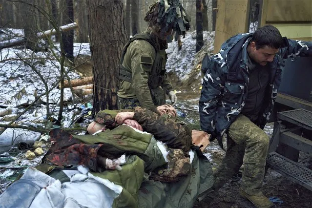 Military medics carry a soldier wounded in a battle to an evacuation vehicle near Kremenna in the Luhansk region, Ukraine, Monday, January 16, 2023. (Photo by LIBKOS/AP Photo)