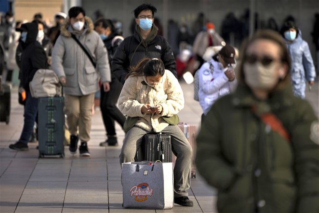 A traveler sits on her suitcase outside the entrance of the Beijing Railway Station in Beijing, Saturday, January 14, 2023. Millions of Chinese are expected to travel during the Lunar New Year holiday period this year. (Photo by Mark Schiefelbein/AP Photo)