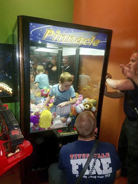 This photo made available by the Titusville Fire and Emergency services shows fire fighters attempting to rescue a boy who crawled inside a claw-style vending machine, Wednesday, February 7, 2018, in Titusville, Fla. The boy sat atop the stuffed toys while firefighters took just 5 minutes to get him out. (Photo by Titusville Fire and Emergency Services via AP Photo)