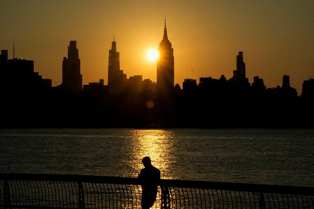 The sun rises behind the Empire State Building and the New York City skyline as a person stands along the riverfront amid an extreme heat warning, in Hoboken, New Jersey, U.S., July 25, 2025. (Photo by Eduardo Munoz/Reuters)