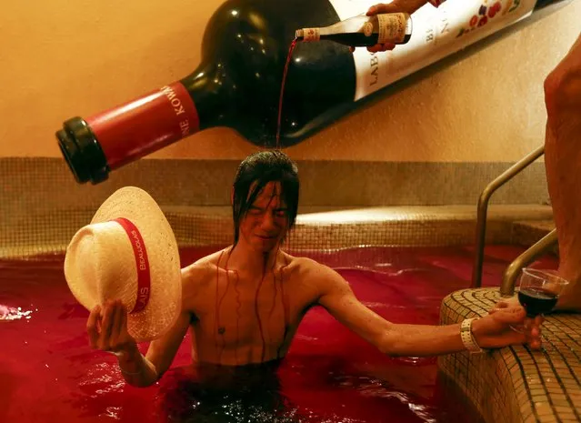 A man pours wine over the head of a customer as he stands in a hot bath with coloured water representing wine at the Hakone Kowaki-en Yunessun spa resort during an event marking Beaujolais Nouveau Day in Hakone west of Tokyo, November 19, 2015. (Photo by Thomas Peter/Reuters)