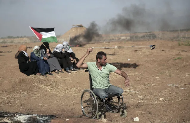 A disabled Palestinian protester hurls stones at Israeli troops during a protest at the Gaza Strip's border with Israel, Friday, May 11, 2018. Gaza activists burned tires near the sealed border with Israel on Friday in a seventh weekly protest aimed at shaking off a decade-old blockade of their territory. Israeli soldiers fired tear gas volleys from the other side of the border fence. (Photo by Khalil Hamra/AP Photo)