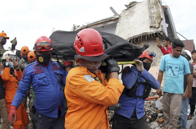 Rescuers carry the body of an earthquake victim retrieved from the ruin of a building damaged by an earthquake in Mamuju, West Sulawesi, Indonesia, Saturday, January 16, 2021. Damaged roads and bridges, power blackouts and lack of heavy equipment on Saturday hampered Indonesia's rescuers after a strong and shallow earthquake left a number of people dead and injured on Sulawesi island. (Photo by Bamu Saseno/AP Photo)