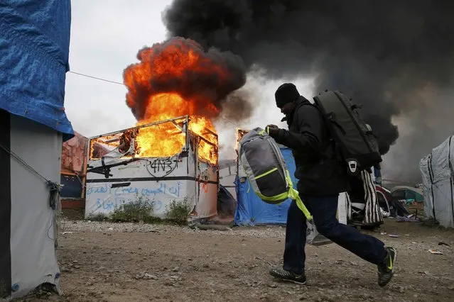 A migrant with his belongings walks past a burning makeshift shelter in the “Jungle” on the third day of their evacuation and transfer to reception centers in France, as part of the dismantlement of the camp in Calais, France, October 26, 2016. (Photo by Pascal Rossignol/Reuters)