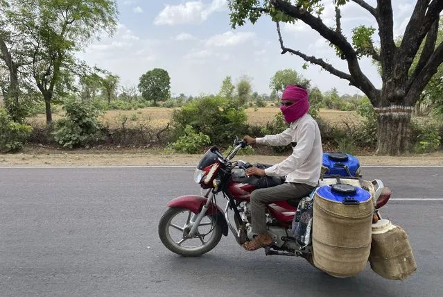 A milkman rides his motorcycle has his containers covered with wet jute sacks to prevent the milk from getting damaged due to excess heat in Lalitpur,  Uttar Pradesh state, India, Saturday, June 17, 2023. At least 34 people have died in the past two days as a large swath of the north Indian state of Uttar Pradesh swelters under severe heat, officials said Saturday, prompting doctors to advise citizens above 60 years of age against venturing out during the daytime. (Photo by Rajesh Kumar Singh/AP Photo)