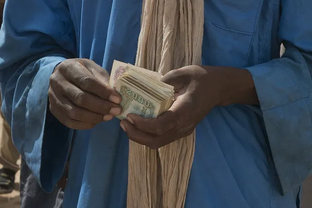 A smuggler counts his money as migrants climb into trucks to head north into Algeria at the Assamaka border post in northern Niger on Sunday, June 3, 2018. The International Organization for Migration has estimated that for every migrant known to have died crossing the Mediterranean, as many as two are lost in the desert. (Photo by Jerome Delay/AP Photo)