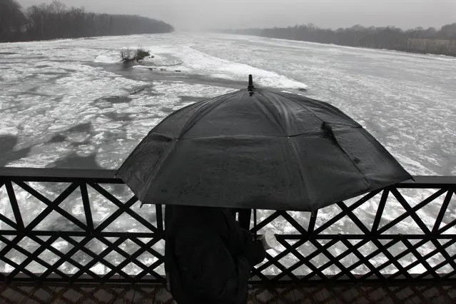 A man uses an umbrella as he walks in the rain on the Calhoun Street Bridge over an ice-clogged Delaware River, Sunday, January 18, 2015, in Trenton, N.J. (Photo by Mel Evans/AP Photo)