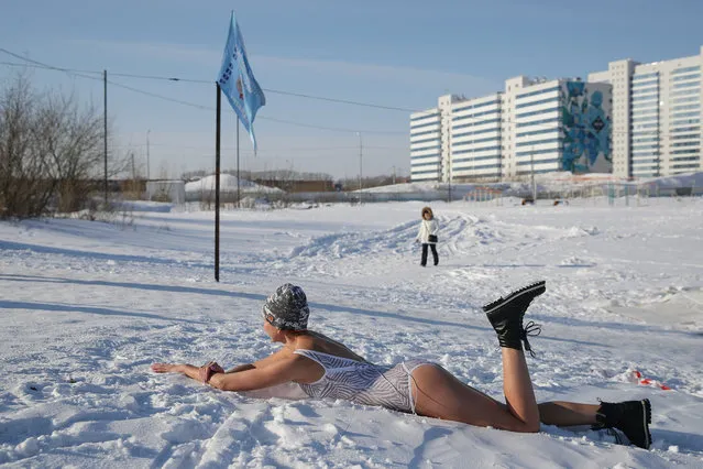 A woman lies on the snow as ice swimmers take turns in a 24-hour swimming session in a pit lake in the Yugo-Zapadny residential estate in the Siberian city of Novosibirsk, Russia on February 27, 2021. The event honours the memory of WWII Soviet infantry soldier Alexander Matrosov who blocked a German machine-gun with his body. (Photo by Kirill Kukhmar/TASS)