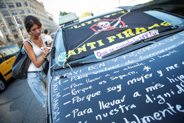 A woman writes a message on a taxi as strikes continue blocking streets in downtown Barcelona, Spain, 01 August 2018. Taxis in Madrid, Barcelona and other cities continue their strike against VTC services Uber and Cabify demanding the Government to regulate them and force them to follow the law. According to the Spanish law there is a maximum of one VTC per 30 taxis, a figure that, according to taxi drivers, is exceeded by both companies. (Photo by Enric Fontcuberta/EPA/EFE)