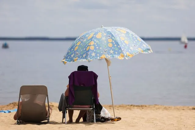 A beachgoer sits in the shade of an umbrella on the beach at the Lac de Cazaux lake, southwestern France, on July 6, 2023, as France braces for a sweltering weekend ahead. (Photo by Thibaud Moritz/AFP Photo)