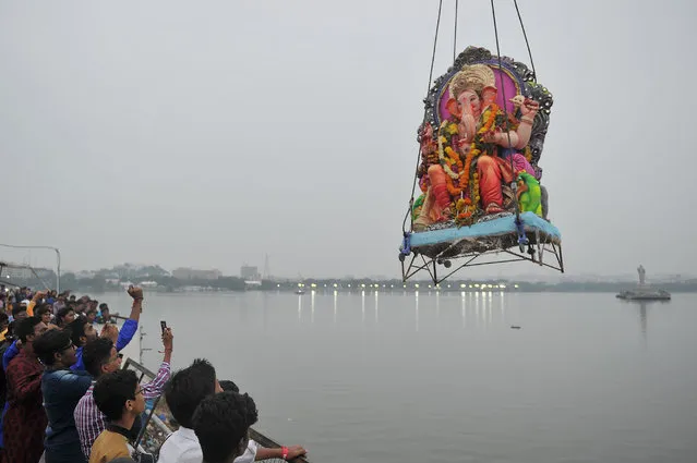 Indian devotees watch as workers use a crane to immerse an idol of Hindu god Lord Ganesh in the Hussain Sagar Lake on the ninth day of the eleven- day long festival Ganesh Chaturthi in Hyderabad on September 21, 2018. The Ganesh Chaturthi festival, a popular 11- day religious festival which is annually celebrated across India, runs this year from September 13 to September 23, and culminates with the immersion of idols of Ganesh in local water bodies. (Photo by Noah Seelam/AFP Photo)