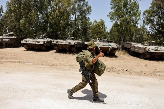 An Israeli soldier gestures as he walks by armoured personnel carriers (APC) near the border between Israel and the Gaza Strip, on its Israeli side, following Israel-Hamas truce on May 21, 2021. (Photo by Ronen Zvulun/Reuters)