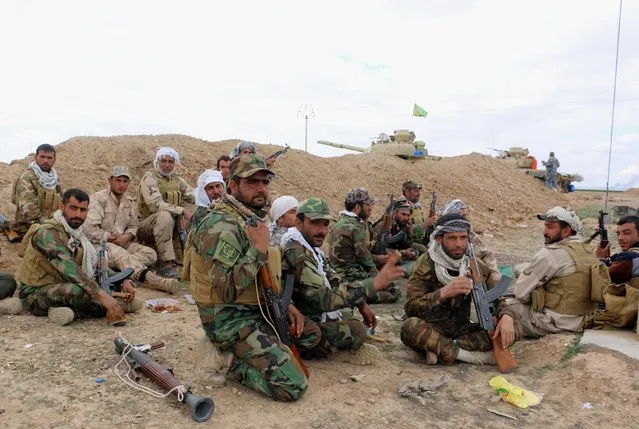 In this Wednesday, March 4, 2015 photo, Shiite militiamen rest behind a sand berm as the Iraqi army, supported by volunteers, battles Islamic State extremists outside Tikrit, 80 miles (130 kilometers) north of Baghdad, Iraq. Iranian-backed Shiite militias and Sunni tribes have joined Iraq's military in a major operation to retake Tikrit from the Islamic State group, while the U.S. led coalition has remained on the sidelines. (AP Photo)