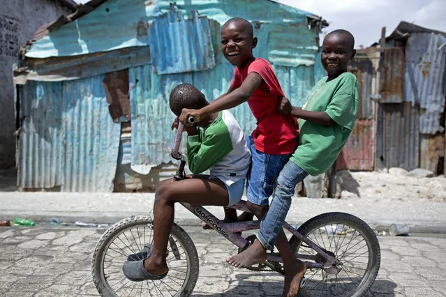 In this June 14, 2018 photo, three children balance themselves on a bicycle as they make their way through the Cite Soleil slum of Port-au-Prince, Haiti. (Photo by Dieu Nalio Chery/AP Photo)