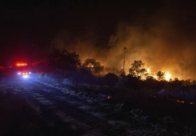 A fire truck approaches as a structure is engulfed in flames as a wildfire called the Highland Fire burns in Aguanga, Calif., Monday, October 30, 2023. A wildfire fueled by gusty Santa Ana winds ripped through rural land southeast of Los Angeles on Monday, forcing thousands of people from their homes, fire authorities said. (Photo by Ethan Swope/AP Photo)