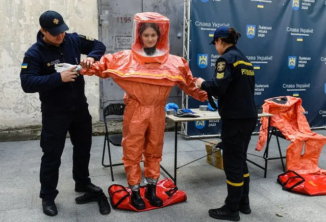 Ukrainian Emergency Ministry rescuers assist a woman to put on protective clothing during a nuclear emergency training session for civilians in the western Ukrainian city of Lviv on September 8, 2022. Kyiv on September 7, called for an international mission to be set up in the Zaporizhzhia nuclear power plant, and called for the population to evacuate the area amid fears of a nuclear disaster. (Photo by Yuriy Dyachyshyn/AFP Photo)