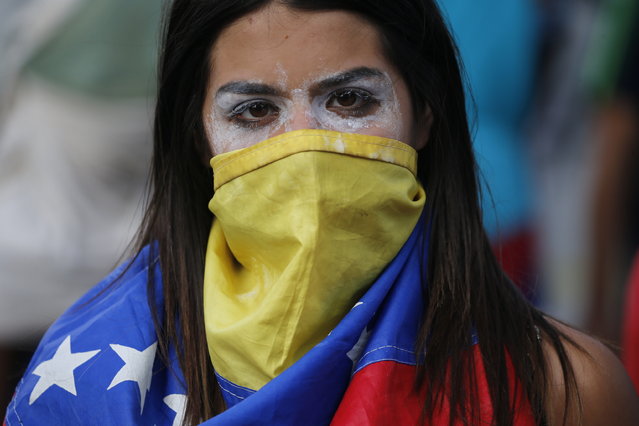 In this Wednesday, January 23, 2019, an anti-government protester covers her face with a Venezuelan flag, and uses toothpaste around her eyes to help lessen the effect of tear gas, during clashes with security forces after a rally demanding the resignation of President Nicolas Maduro in Caracas, Venezuela. The head of Venezuela's opposition-run congress declared himself interim president at the rally, until new elections can be called. (Photo by Fernando Llano/AP Photo)