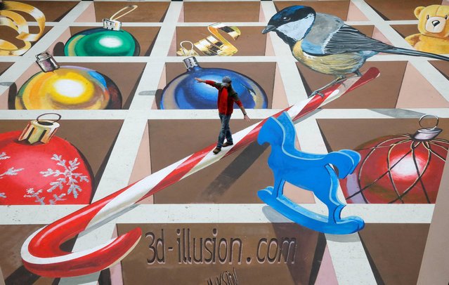 A man poses on a 3-dimensional picture during the presentation of Ukraine's largest 3D street painting in “Olimpiysky” stadium in Kiev, Ukraine, Tuesday January 14, 2014. The 421 square meters picture is created by Ukrainian artist Alex Maksimov. (Photo by Efrem Lukatsky/AP Photo)