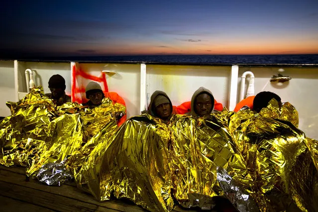 Sub-Saharan migrants cover themselves with a heating blanket at the deck of the Golfo Azzurro boat after been rescued from a rubber boat by members of Proactive Open Arms NGO, at the Mediterranean sea, about 24 miles north of Sabratha, Libya, on Friday, January 27, 2017. Rescuers pulled nearly 300 people from two rubber boats in waters off the Libyan coast on Friday and were looking for 100 more believed to be on a another boat missing since Sunday. (Photo by Emilio Morenatti/AP Photo)