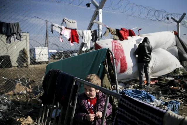 An Iraqi refugee boy of the Yazidi faith stands next to the border fence at the Greek-Macedonian border, at a makeshift camp for refugees and migrants near the village of Idomeni, Greece, March 19, 2016. (Photo by Alkis Konstantinidis/Reuters)