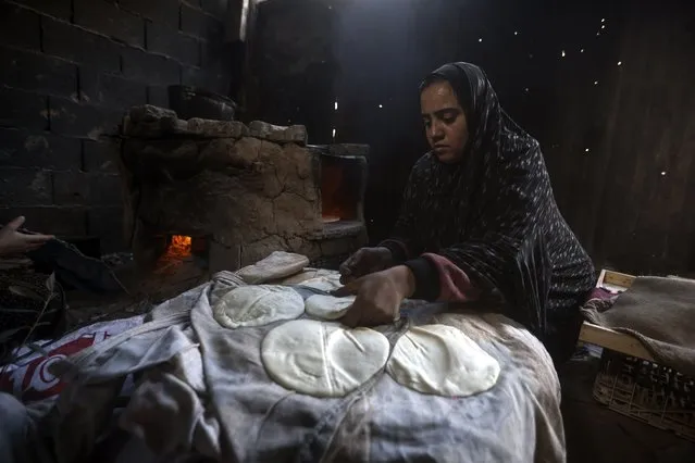 A Palestinian woman displaced by the Israeli ground offensive on the Gaza Strip bake bread at a makeshift tent camp in Rafah, Gaza Strip, Monday, February 19, 2024. (Photo by Mohammed Dahman/AP Photo)