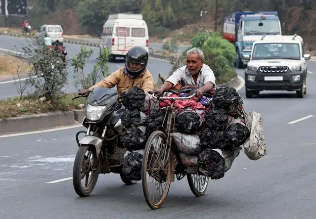 A motorcyclist pushes a man on a bicycle loaded with coal bags on the outskirts of Ranchi, India, on February 27, 2024. (Photo by Amit Dave/Reuters)