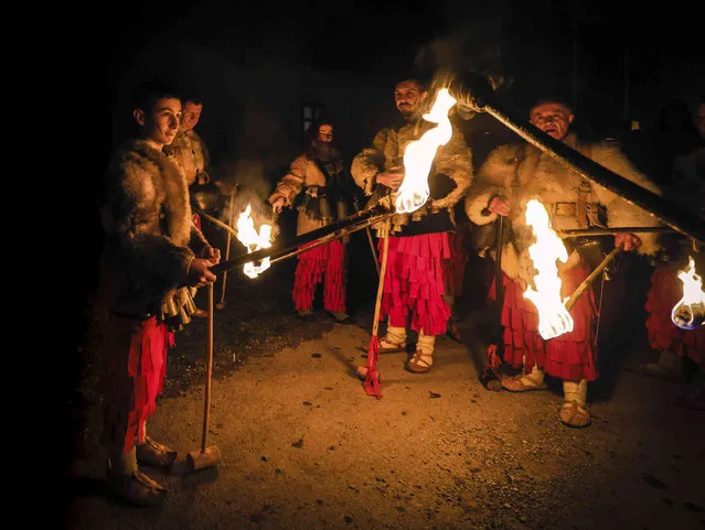 Dancers light their torches as they perform an age-old ritual chasing the evil spirits away on the streets of Donna Sekirna, Bulgaria, late Friday, January 13, 2023. Every winter in villagers in western Bulgaria donning large, frightening masks depicting mythical creatures took to the streets Friday, in an age-old Orthodox New Year carnival believed to ward off evil spirits. (Photo by Valentina Petrova/AP Photo)