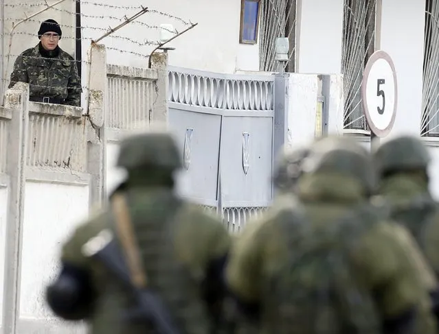 A Ukrainian serviceman watches uniformed men, believed to be Russian servicemen, passing by at a Ukrainian military base in the village of Perevalnoye outside Simferopol, March 6, 2014. Crimea's parliament voted to join Russia on Thursday and its Moscow-backed government set a referendum within 10 days on the decision in a dramatic escalation of the crisis over the Ukrainian Black Sea peninsula. (Photo by Vasily Fedosenko/Reuters)