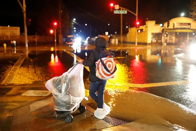 A woman with her shoes and belongings wrapped in plastic bags looks at the flooded East Santa Clara Street as water continues to rise after heavy rains overflowed nearby Coyote Creek in San Jose, California, U.S. February 21, 2017. (Photo by Stephen Lam/Reuters)