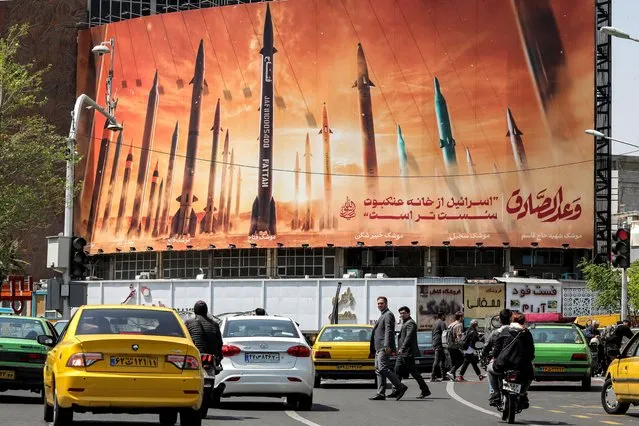 Motorists drive their vehicles past a billboard depicting named Iranian ballistic missiles in service, with text in Arabic reading “the honest (person's) promise” and in Persian “Israel is weaker than a spider's web”, in Valiasr Square in central Tehran on April 15, 2024. Iran on April 14 urged Israel not to retaliate militarily to an unprecedented attack overnight, which Tehran presented as a justified response to a deadly strike on its consulate building in Damascus. (Photo by Atta Kenare/AFP Photo)