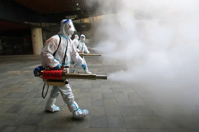 Staff members wearing personal protective equipment (PPE) spray disinfectant outside a shopping mall in Xi'an in north China's Shaanxi province on January 11, 2022. (Photo by AFP Photo/China Stringer Network)