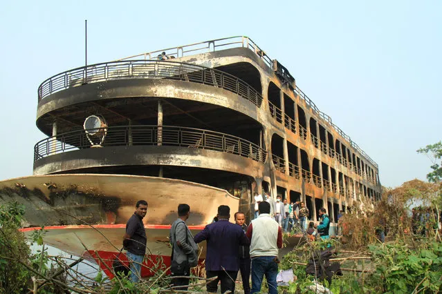 People look at the burnt-out ferry as it is anchored along a coast a day after it caught on fire killing at least 37 people in Jhalkathi, 250 kilometres (160 miles) south of Dhaka, on December 24, 2021. (Photo by Arifur Rahman/AFP Photo)