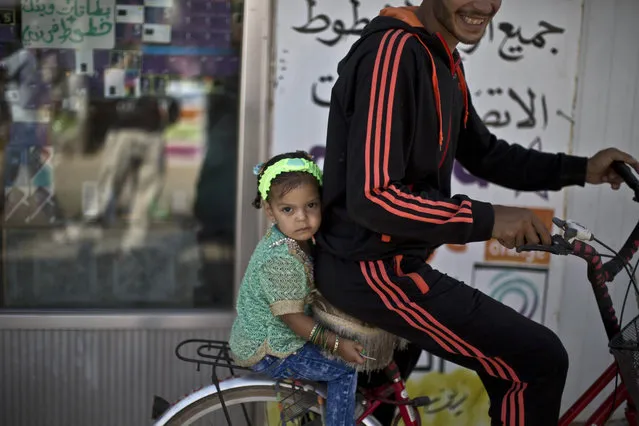 A Syrian man and his daughter ride a bicycle while celebrating the first day of the Eid al-Fitr holiday that marks the end of the holy fasting month of Ramadan at Zaatari refugee camp, in Mafraq, Jordan, Friday, July 17, 2015. (Photo by Muhammed Muheisen/AP Photo)