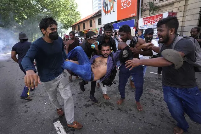 An injured student is carried by colleagues as police fire tear gas and water cannons to disperse protesting members of the Inter University Students Federation during an anti government protest in Colombo, Sri Lanka, Thursday, May 19, 2022. (Photo by Eranga Jayawardena/AP Photo)