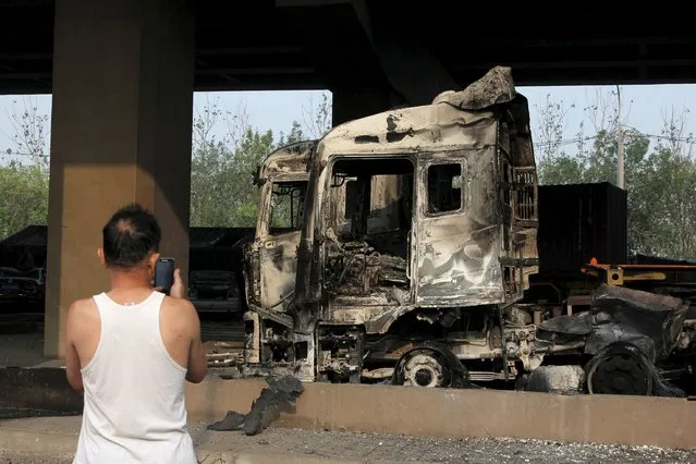A man takes pictures of a damaged vehicle under a bridge near the site of the explosions at the Binhai new district in Tianjin August 13, 2015. (Photo by Reuters/Stringer)