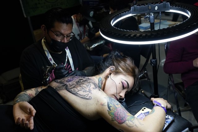 A tattoo artist works on a woman´s back during a tattoo convention at the World Trade Center in Mexico City, Sunday, August 20, 2023. Tattoo artists from Costa Rica, Mexico, Brazil, the US, and Colombia are gathering for two days in Mexico. (Photo by Arnulfo Franco/AP Photo)