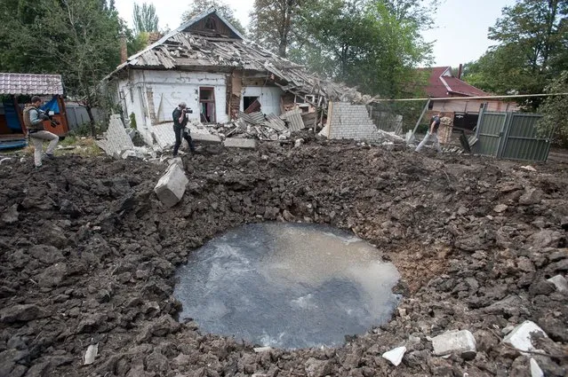Journalists walk near a crater caused by a shell which damaged a house following fighting between pro-Russian rebels and Ukrainian government forces in Shakhtarsk, Donetsk region, eastern Ukraine, Thursday, Aug. 7, 2014. (Photo by Evgeniy Maloletka/AP Photo)