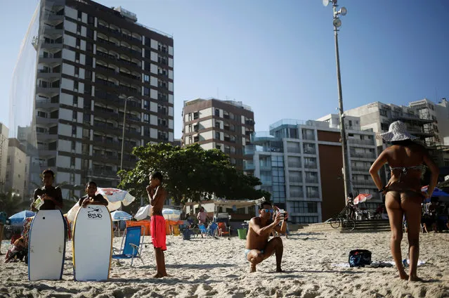 A tourist (2nd R) takes a picture of a woman, as boys who are residents of Cantagalo favela stand nearby, on Ipanema beach in Rio de Janeiro, Brazil, May 3, 2016. (Photo by Nacho Doce/Reuters)