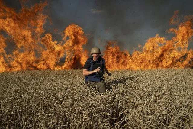 Photojournalist Evgeniy Maloletka runs from a blaze in a burning wheat field while on assignment after Russian shelling, a few kilometers from the Ukrainian-Russian border in the Kharkiv region, Ukraine, Friday, July 29, 2022. (Photo by Mstyslav Chernov/AP Photo)