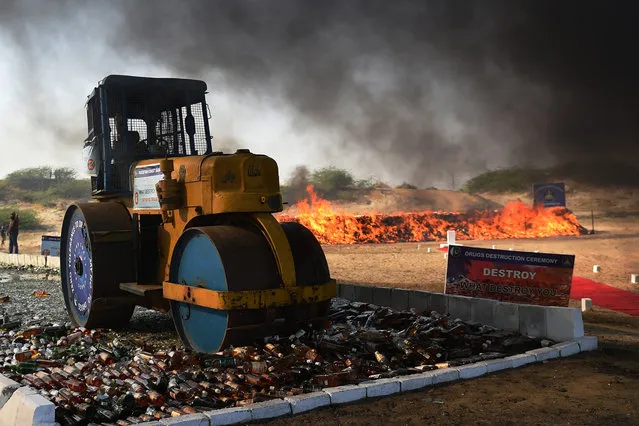 A Pakistani official uses a steamroller to crush bottles of liquor beside burning drugs on the outskirts of Karachi on February 20, 2020, during an event organized by the Pakistan Coast Guards to destroy seized illicit alcohol and drugs smuggled into the country. (Photo by Rizwan Tabassum/AFP Photo)