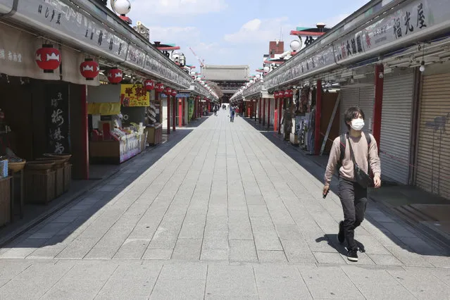 A man wearing face mask to protect against the spread of the new coronavirus walks through deserted Nakamise alley in Asakusa, Tokyo, Wednesday, April 8, 2020. Prime Minister Shinzo Abe declared Tuesday a monthlong state of emergency in Tokyo and six other prefectures because of a spike of infections in the country with the world's oldest population. (Photo by Koji Sasahara/AP Photo)
