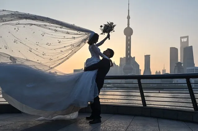 A couple poses for a wedding photo shoot on the Bund promenade along the Huangpu River during sunrise in Shanghai on September 7, 2022. (Photo by Hector Retamal/AFP Photo)