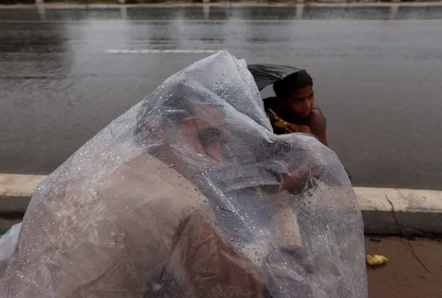 A man uses a plastic sheet as he sells grilled corn in the rain in New Delhi, India August 1, 2016. (Photo by Adnan Abidi/Reuters)