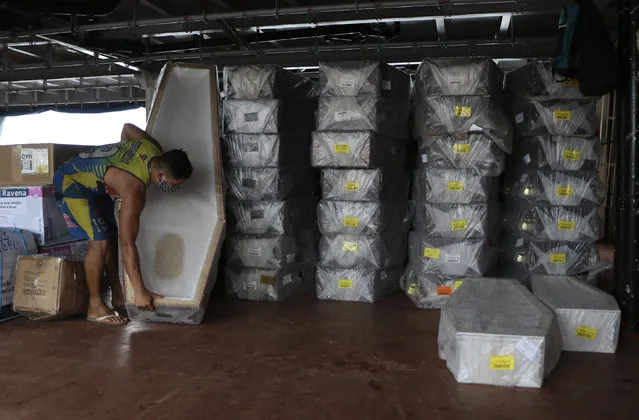 A docker helps to unload hundreds of coffins from the boat Amazon Star, at the Roadway port in Manaus, Amazonas state, Brazil, Friday, May 8, 2020. In Brazil’s bustling Amazon city of Manaus, so many people have died within days in the new coronavirus pandemic that the coffins are running out. (Photo by Edmar Barros/AP Photo)