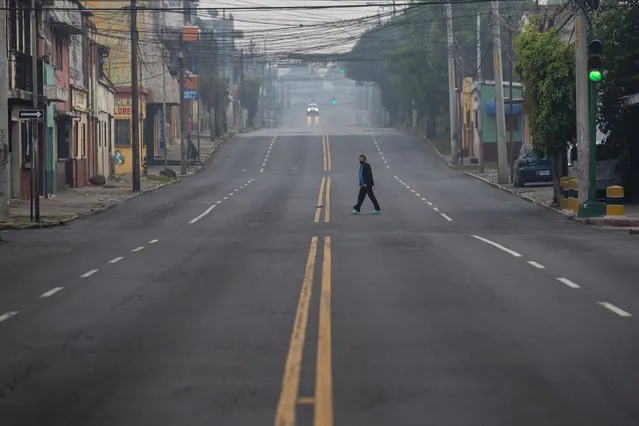 A woman crosses an street that's empty due to a tight lockdown in Guatemala City, early Friday, May 15, 2020. The government decreed a three-day, nationwide lockdown starting Friday to help contain the spread of the new coronavirus. (Photo by Moises Castillo/AP Photo)