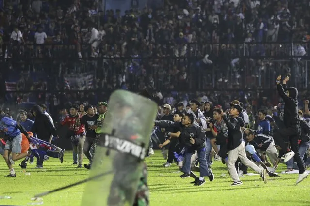 Soccer fans enter the pitch during a clash between supporters at Kanjuruhan Stadium in Malang, East Java, Indonesia, Saturday, October 1, 2022. Clashes between supporters of two Indonesian soccer teams in East Java province killed over 100 fans and a number of police officers, mostly trampled to death, police said Sunday. (Photo by Yudha Prabowo/AP Photo)