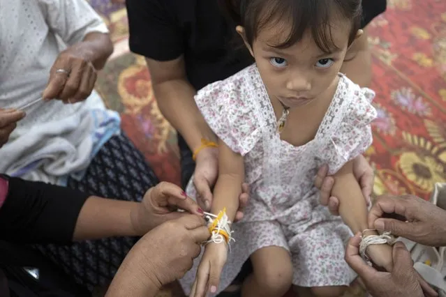 Relatives of the victims of the mass killing attack tie holy threads on the wrists of 3 year old Paweenuch Supolwong, the only child to emerge unscathed, inside Wat Rat Samakee temple in Uthai Sawan, north eastern Thailand, Saturday, October 8, 2022. A former police officer burst into a day care center in northeastern Thailand on Thursday, killing dozens of preschoolers and teachers before shooting more people as he fled. (Photo by Wason Wanichakorn/AP Photo)