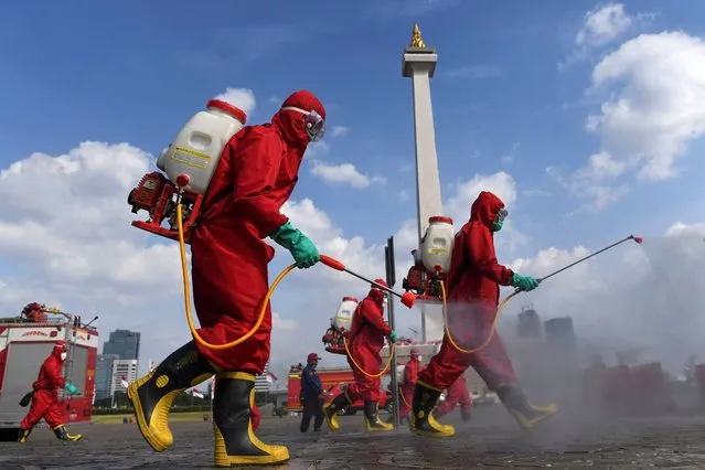 Firefighters wearing protective suits spray disinfectant at the National Monument area to prevent the spread of the coronavirus disease (COVID-19) in Jakarta, Indonesia on June 17, 2020. (Photo by Wahyu Putro/Antara Foto via Reuters)