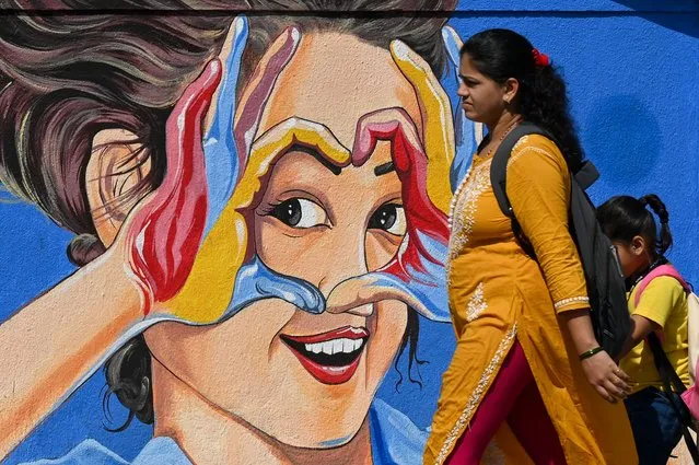 A woman along with a child walk past a wall mural in Mumbai on November 29, 2022. (Photo by Punit Paranjpe/AFP Photo)